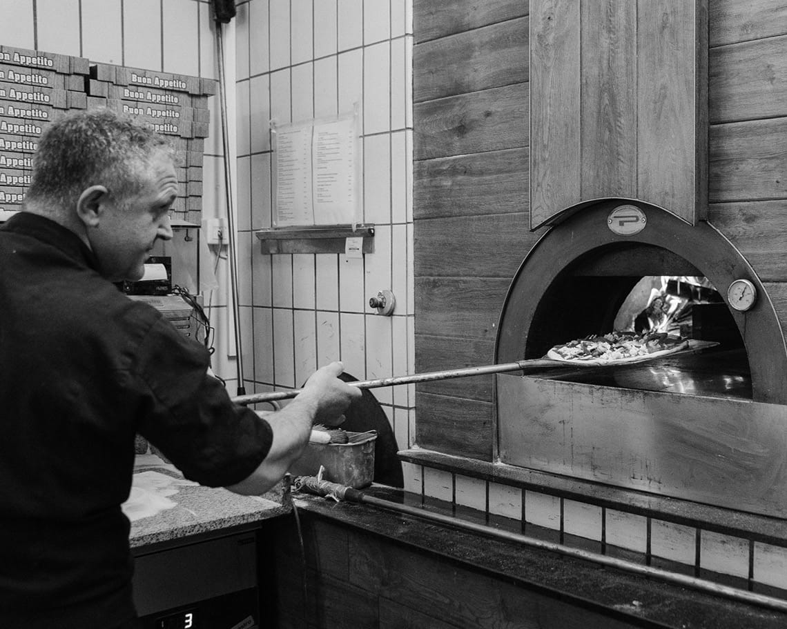 Pizza wird in den Holzofen geschoben